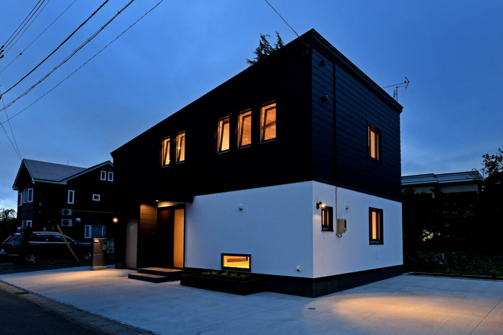夕景に浮かぶ黒と白の外壁を持つ、借景を楽しむ家の外観